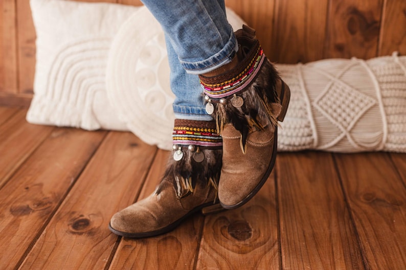 May include: Brown suede ankle boots with decorative feather and beaded trim. The boots are worn with blue jeans.