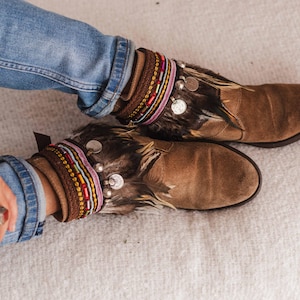 May include: Brown suede ankle boots with feather and beaded embellishments. The boots have a pointed toe and a low heel.