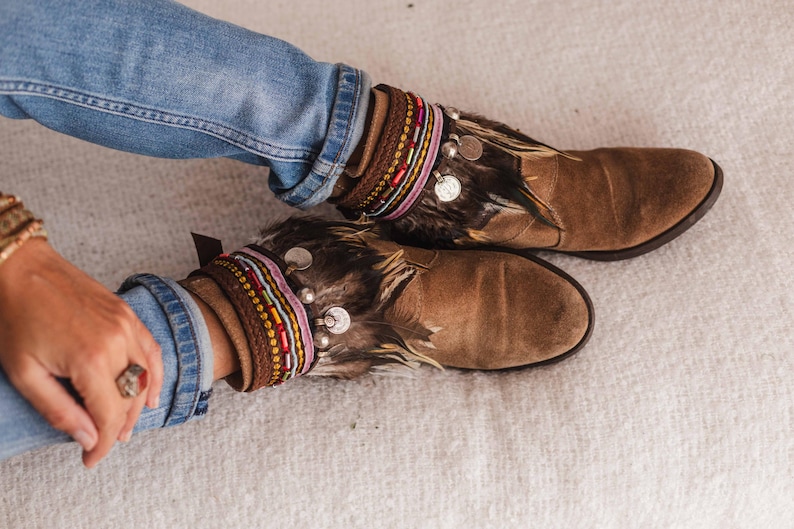 May include: Brown suede ankle boots with feather and beaded embellishments. The boots have a pointed toe and a low heel.