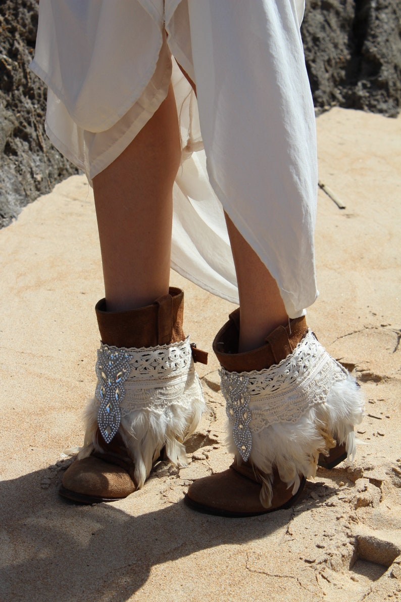 Handmade feather bridal shoe cuffs with ivory feathers, Swarovski crystal applique, and soft cotton trims. These boho wedding boot covers add sparkle and charm to bridal boots, sandals, or festival shoes. Adjustable buckle strap for comfort, unique boho accessory, perfect for brides, bridesmaids, or gifts