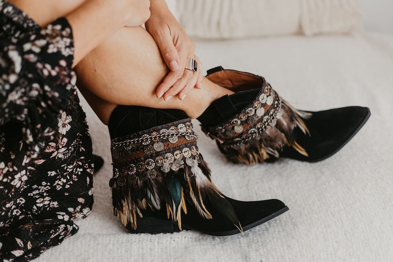 Handmade boho tribal feather boot covers with embroidered trim, metal coins and chain, styled on black boots.