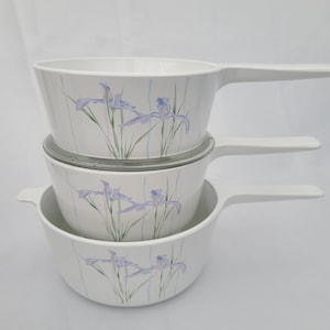 May include: A set of three white ceramic bowls with a floral design. The bowls have a white background with a light blue and green floral pattern. The bowls are stacked on top of each other.