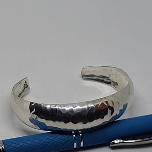 May include: A silver hammered bangle bracelet. The bracelet is open and has a smooth, rounded finish.