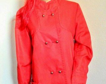 May include: A red long-sleeved coat with a double-breasted closure and four gold buttons. The coat has a pocket on the left side and a mandarin collar.