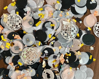 May include: A collection of party confetti in various shapes and colors. The confetti includes black, white, and translucent circles, along with gold and yellow accents. Several white disco ball shapes are scattered throughout the confetti.