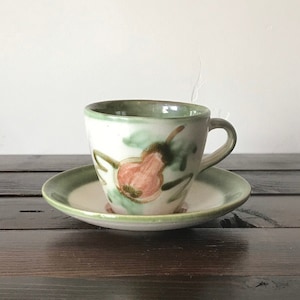 May include: A green and white ceramic teacup and saucer with a floral design. The cup has a handle and the saucer has a rim.
