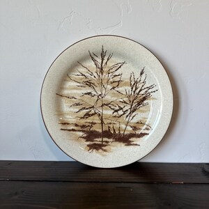 May include: A brown and white ceramic dinner plate with a brown silhouette of tall grass on a beige background.