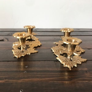 May include: A set of three gold metal candle holders with a leaf design. Each holder has a round top and a base with a leaf design.