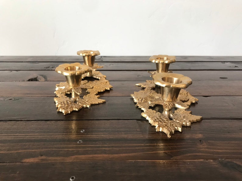 May include: A set of three gold metal candle holders with a leaf design. Each holder has a round top and a base with a leaf design.