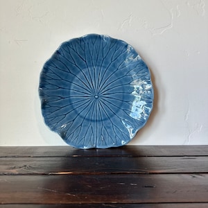 May include: A blue ceramic plate with a lotus leaf design. The plate has a scalloped edge and a raised design.