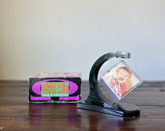 May include: A black plastic stand with a clear cube that holds a photo. The cube rotates. The box for the stand says "Magic Photo Cube for 6 Photos".