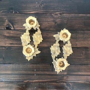 May include: Two gold candle holders with a floral design. Each holder has three candle cups.