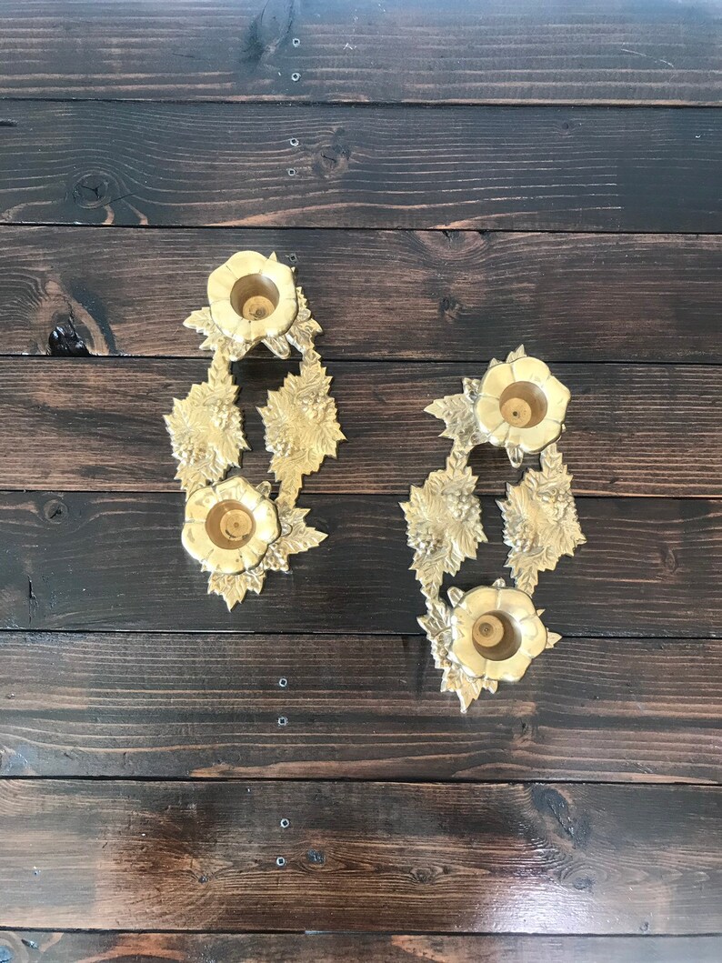 May include: Two gold candle holders with a floral design. Each holder has three candle cups.