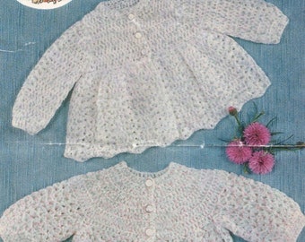May include: Two white crocheted cardigans with long sleeves and round necklines. Each garment features a front button closure with three small white buttons. The knit pattern is open and textured, showing subtle flecks of pink and blue throughout.