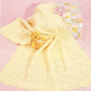May include: A pale yellow knitted baby blanket with a delicate openwork pattern and a scalloped edge. A small, plush yellow chick toy with a white bow around its neck sits on top of the blanket, which is partially draped over a square gift box.