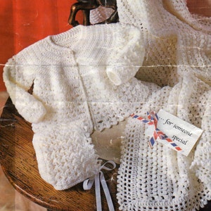 May include: A white crocheted set consisting of a long-sleeved cardigan, a bonnet with white ribbon ties, and a blanket. A small rectangular tag is attached to the blanket with a red, white, and blue striped ribbon, featuring the text ...for someone special.