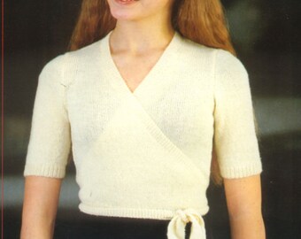 May include: A cream-colored knit wrap top featuring short sleeves, a V-neckline, and a side tie closure. The garment is constructed with a fine-gauge knit texture, ribbed sleeve cuffs, and a ribbed hemline that sits at the waist with a tied bow.