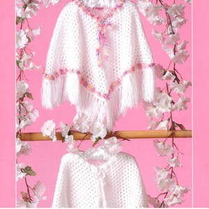 Könnte beinhalten: Zwei weiße gehäkelte Ponchos mit V-förmigem Ausschnitt und Saum. Die Ponchos sind mit einer mehrfarbigen Garnborte in Rosa-, Lila- und Orangetönen verziert und an den unteren Kanten mit langen weißen Fransen versehen.
