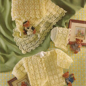 Könnte beinhalten: Ein hellgelbes Häkelset für Babys, bestehend aus einer Decke mit dekorativem Wellenrand, einer passenden langärmeligen Strickjacke mit drei kleinen Knöpfen und einer Haube. Die Teile weisen ein strukturiertes Durchbruchmuster auf.