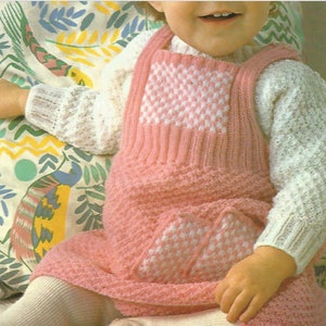 Pode incluir: Um vestido de malha rosa e branco com um padrão de textura, um peitilho quadrado com design xadrez e um bolso frontal a condizer. A peça é usada sobre uma camisola branca de manga comprida com um padrão de malha texturizado.