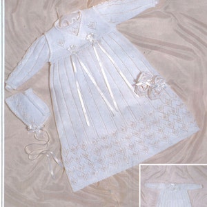 May include: A white knitted long-sleeve gown with a matching bonnet and booties. The gown features vertical ribbing, a chevron-patterned hem, and satin ribbon accents. The text 3 Ply is visible in the top right corner. A smaller inset image shows the full gown.