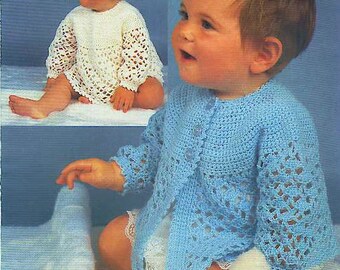 May include: A light blue crocheted cardigan with long sleeves and a delicate openwork pattern, featuring a round neckline and three small buttons down the front. The garment is shown alongside a white crocheted dress with similar openwork details.