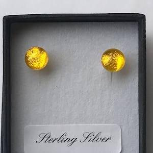May include: A pair of gold-toned earrings with a round, textured design. The earrings are in a black box with a white label that reads "Sterling Silver".