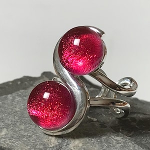 May include: A silver ring with two red glass stones. The ring is designed with a curved, twisted band.