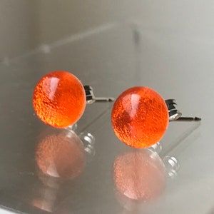 May include: A pair of orange glass stud earrings with silver posts.