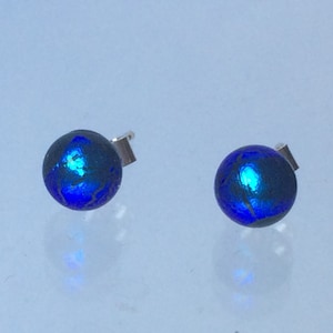 Pode incluir: Um par de brincos de vidro azul com postes de prata. O vidro é iridescente e tem uma superfície texturizada.