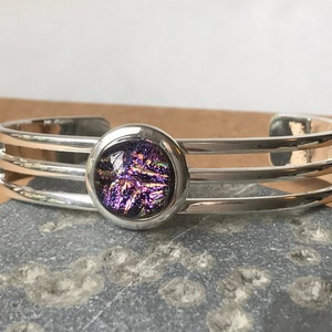 Könnte beinhalten: Silberarmband mit drei Bändern und einem runden, violetten dichroitischen Glascabochon.