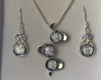 May include: A silver-toned jewelry set featuring a necklace and matching earrings. The necklace has a pendant with three textured, spherical accents. The earrings have a similar design with a single sphere. The set is displayed in a white box.