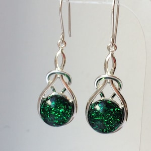May include: A pair of silver dangle earrings with green glitter-filled round glass cabochons. The earrings feature a Celtic knot design.