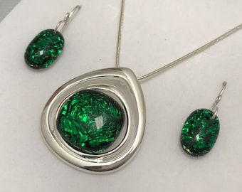 Puede incluir: Un conjunto de collar y pendientes de plata con colgantes de vidrio verde. El collar presenta un colgante en forma de lágrima con un centro de vidrio verde rodeado por dos anillos de plata.