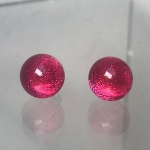 May include: A pair of pink glass stud earrings with a sparkly finish.