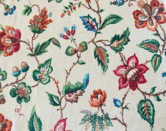 May include: Cream-colored fabric with a repeating floral pattern. The design features large, stylized flowers in shades of red, orange, and pink, with green leaves and blue accents. The floral pattern is set against a neutral background.