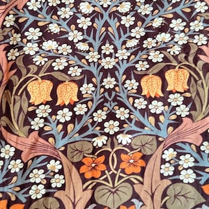 May include: Close-up of a fabric with a repeating floral pattern. The design features white daisy-like flowers, orange bell-shaped flowers, and orange and brown leaves and stems against a dark brown background. The pattern has a vintage aesthetic.