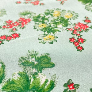May include: A light blue fabric with a repeating pattern of green leaves and red flowers. The fabric has a subtle texture.