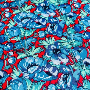 Könnte beinhalten: Ein lebendiges Blumenmuster mit großen blauen Blüten mit weißen Akzenten und grünen Blättern auf einem leuchtend roten Hintergrund. Das Design ist ein sich wiederholendes Muster aus stilisierten Blüten und Blättern, das ein auffälliges Textildesign erzeugt.