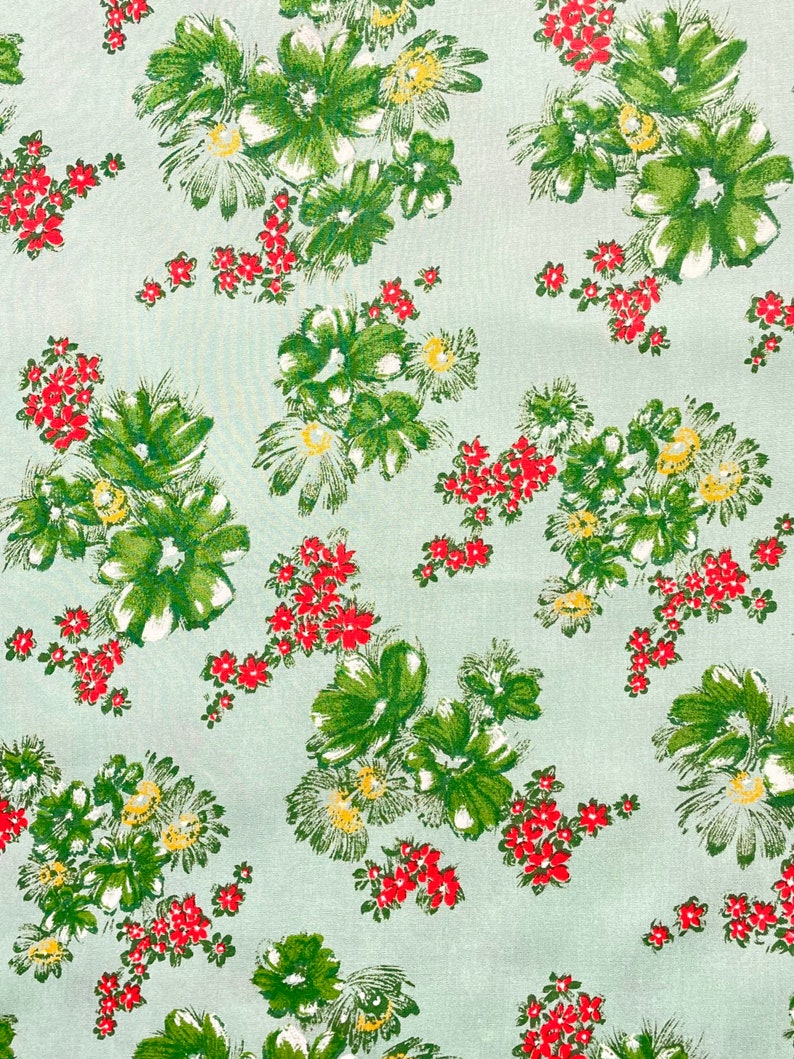 May include: A light blue fabric with a repeating pattern of green and white flowers with red accents.