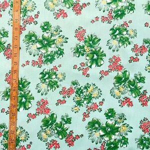 May include: A light blue fabric with a repeating pattern of green and white flowers with red accents.