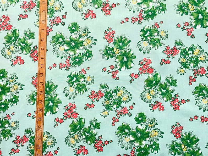 May include: A light blue fabric with a repeating pattern of green and white flowers with red accents.