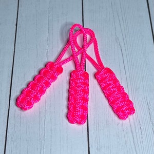 May include: Three pink zipper pulls made of braided cord. The pulls are tied together at the top.