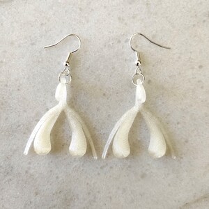 May include: A pair of white dangle earrings with a unique shape. The earrings are made of a smooth, shiny material and have a silver hook.