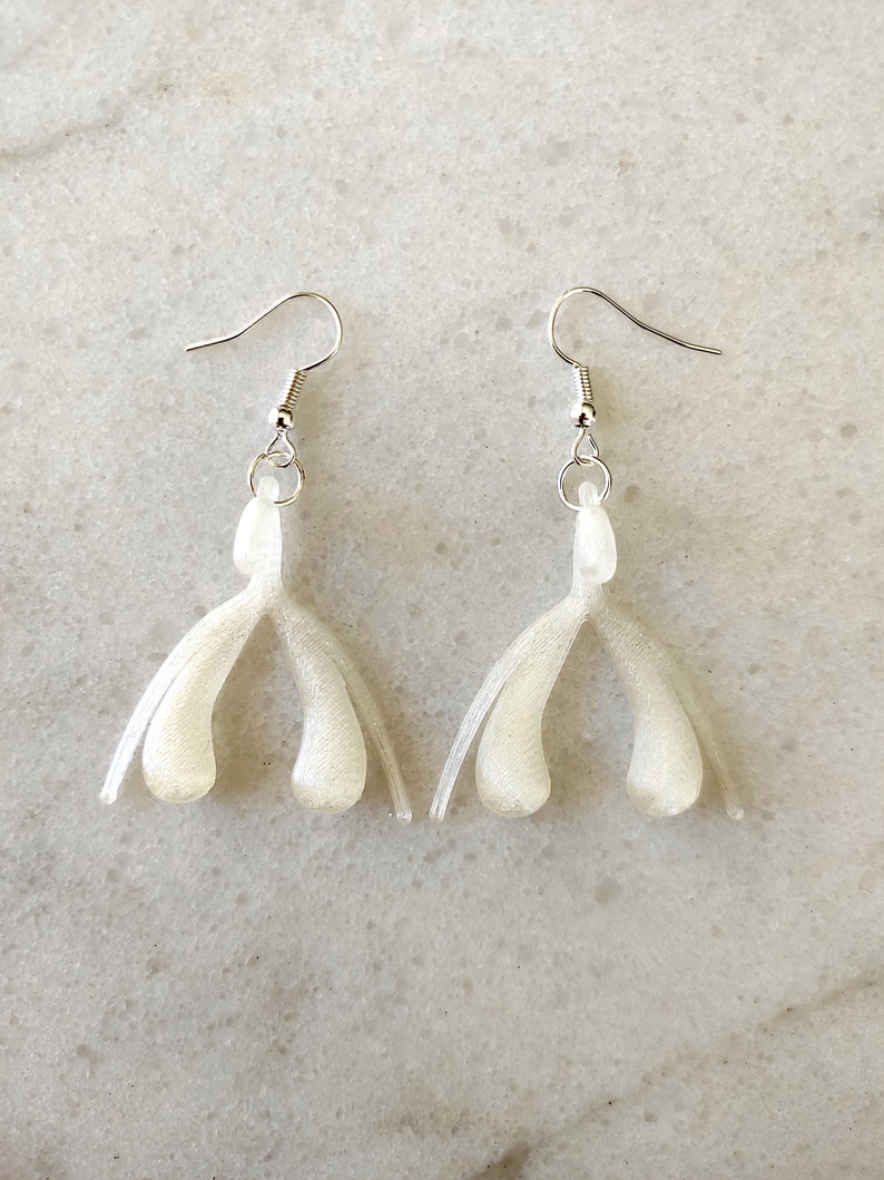 May include: A pair of white dangle earrings with a unique shape. The earrings are made of a smooth, shiny material and have a silver hook.