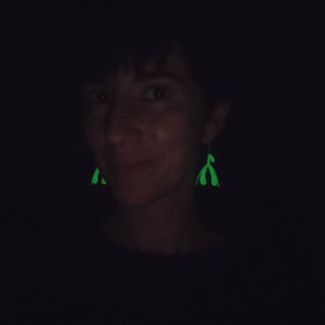 May include: A person wearing a black shirt with green glow-in-the-dark earrings shaped like a pair of hands.