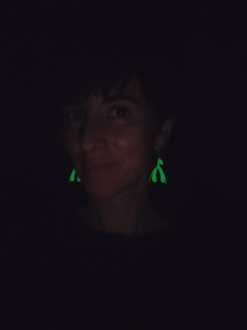 May include: A person wearing a black shirt with green glow-in-the-dark earrings shaped like a pair of hands.