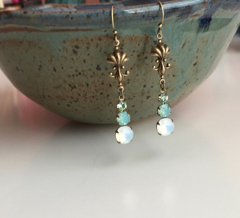May include: A pair of dangle earrings with a fleur-de-lis charm and three crystal beads in shades of light blue and white.
