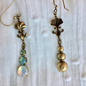 May include: A pair of gold tone dangle earrings with a floral design and three round iridescent stones. The stones are a light green, a light blue, and a white opal.