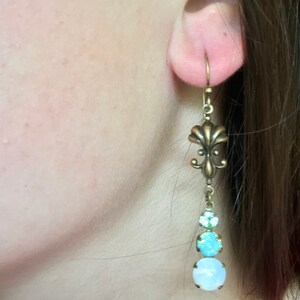 May include: Brass earrings with a fleur-de-lis design and three round, iridescent stones in shades of blue and white.